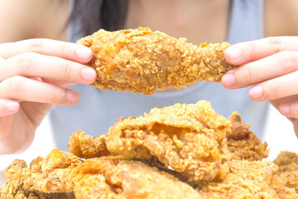 Woman holding and eatting fried chicken in white plate on white table