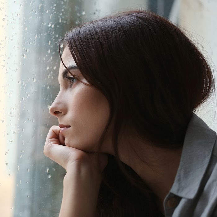 Depressed young woman near window at home
