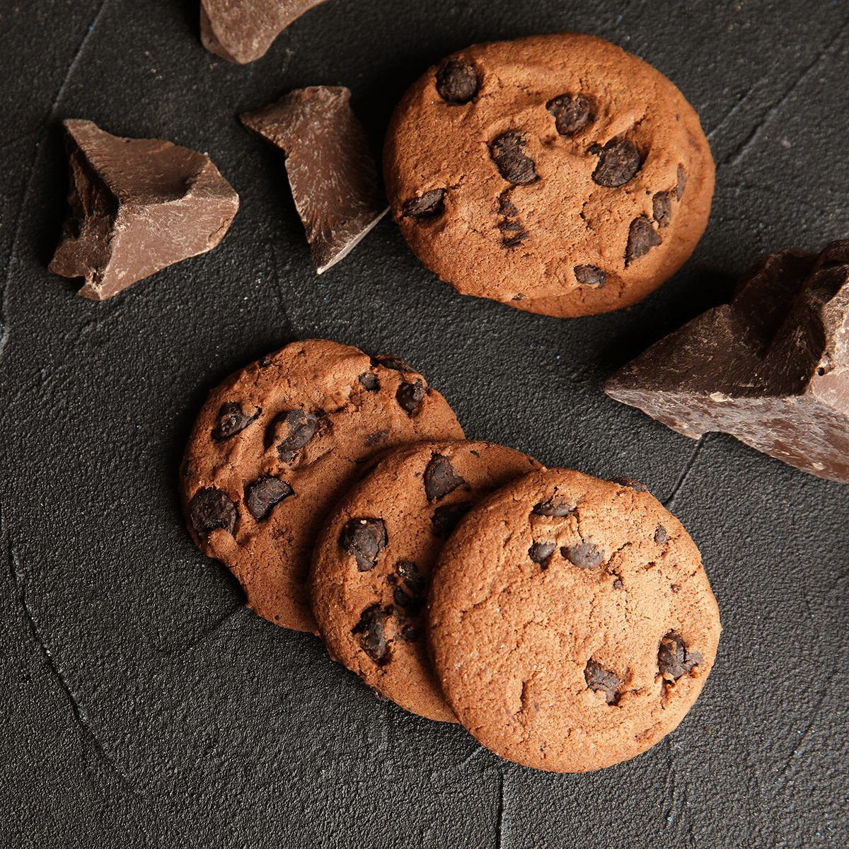 Tasty chocolate chip cookies on dark background, flat lay.