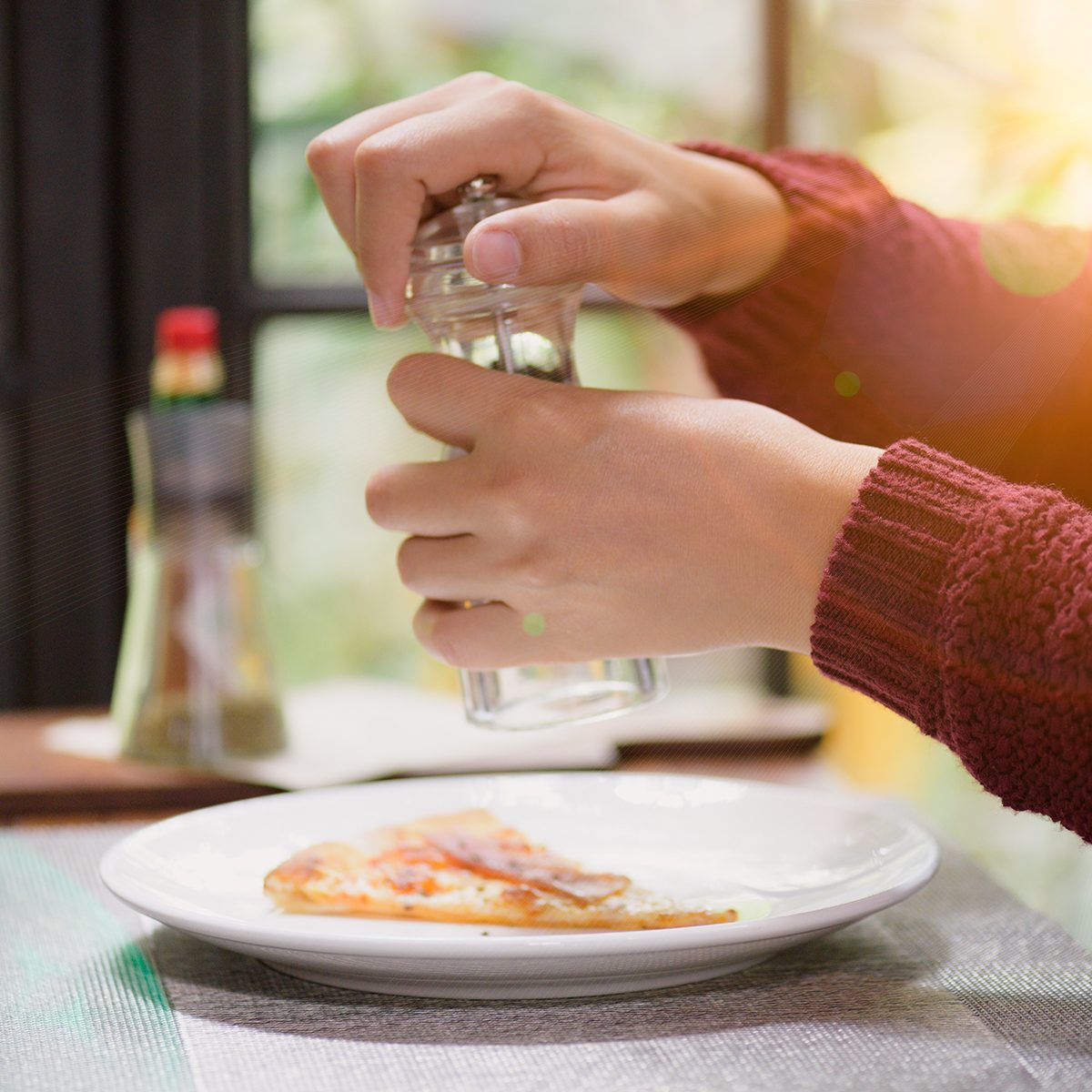 Woman hands using black pepper and salt shaker on the slices of pizza