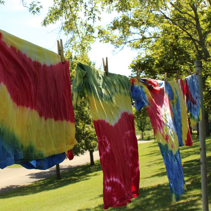 Multi colored tie dye tee shirts hanging on clothesline with trees