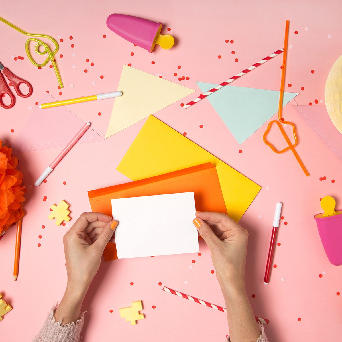 Top view flat lay with feminine hands holding empty greeting card on bright pink background.