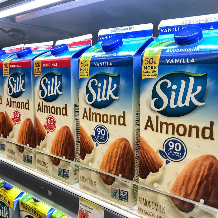 Cartons of almond milk stand on a shelf in a supermarket.