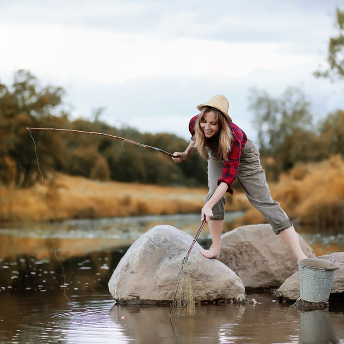 Beautiful young girl in autumn by the river with a fishing rod