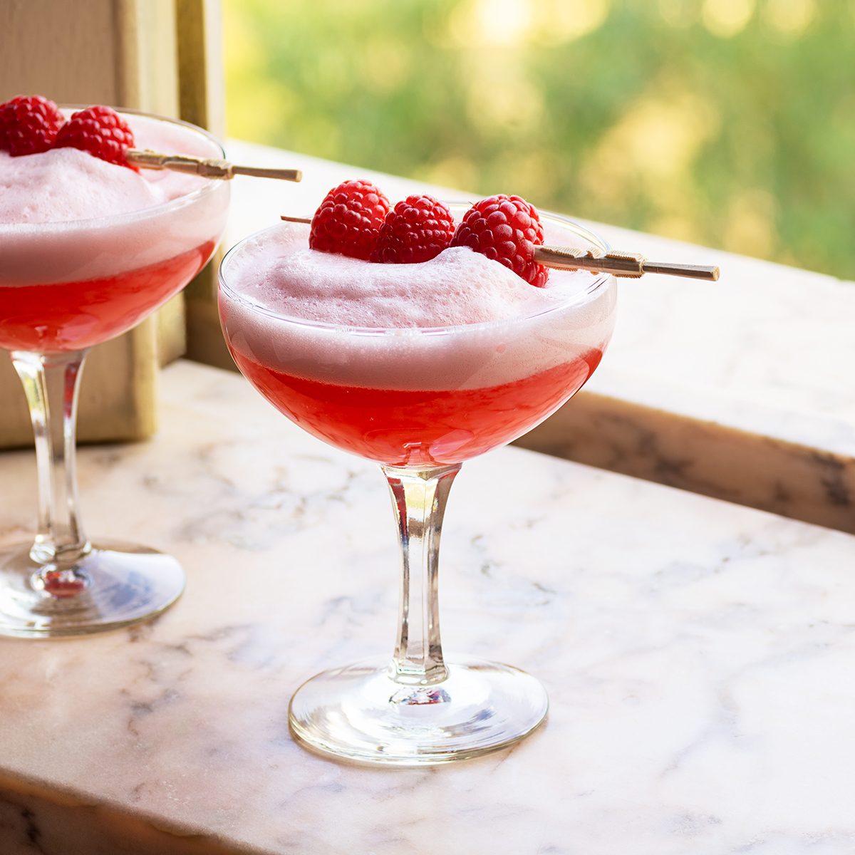 Red Clover Club Cocktails with Layered Egg White Foam and Raspberry Garnish in Marble Windowsill