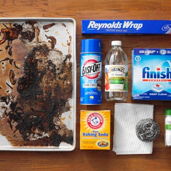 dirty baking sheet next to various cleaning supplies on a wood butcher block background