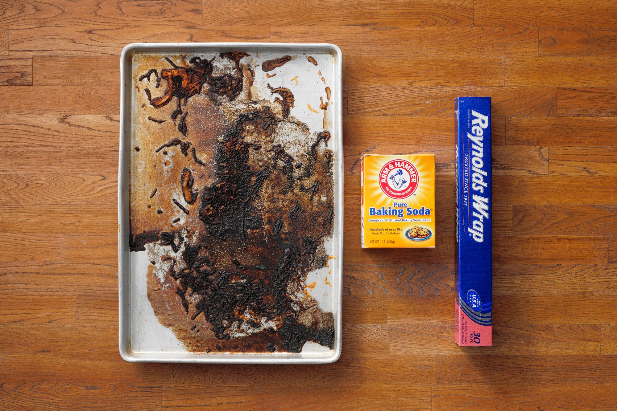 dirty baking sheet next to a box of baking soda and aluminum foil on wood butcher block background
