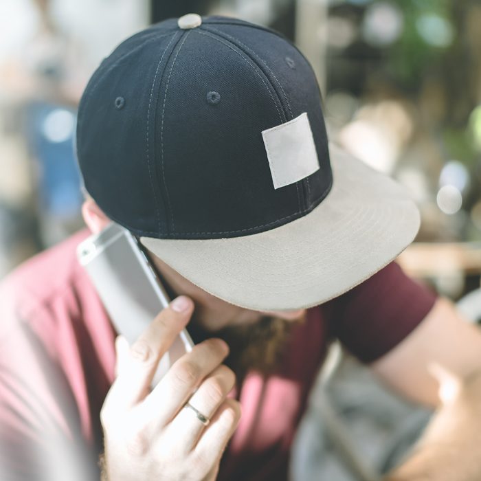 Closeup of a baseball cap with space for text. A man in a cap with a visor sitting with his head down and talking on the phone. Man uses the gadget.