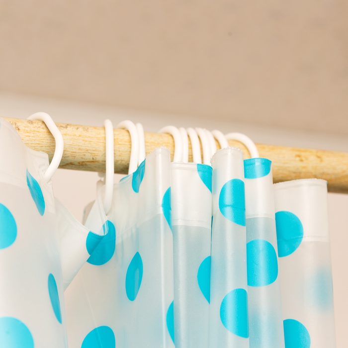 cream curtains hanging on the rope on the plastic hook in the white ceiling illuminated by daylight