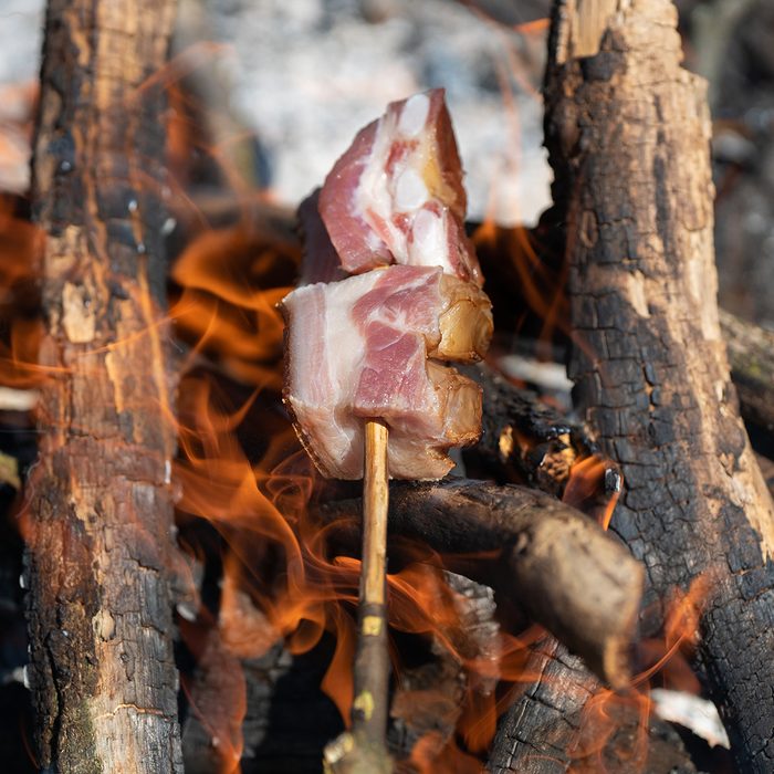 bacon baking spit on fire barbecue camping in the nature stock photo