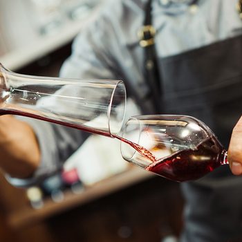 Sommelier pouring wine into glass from mixing bowl.