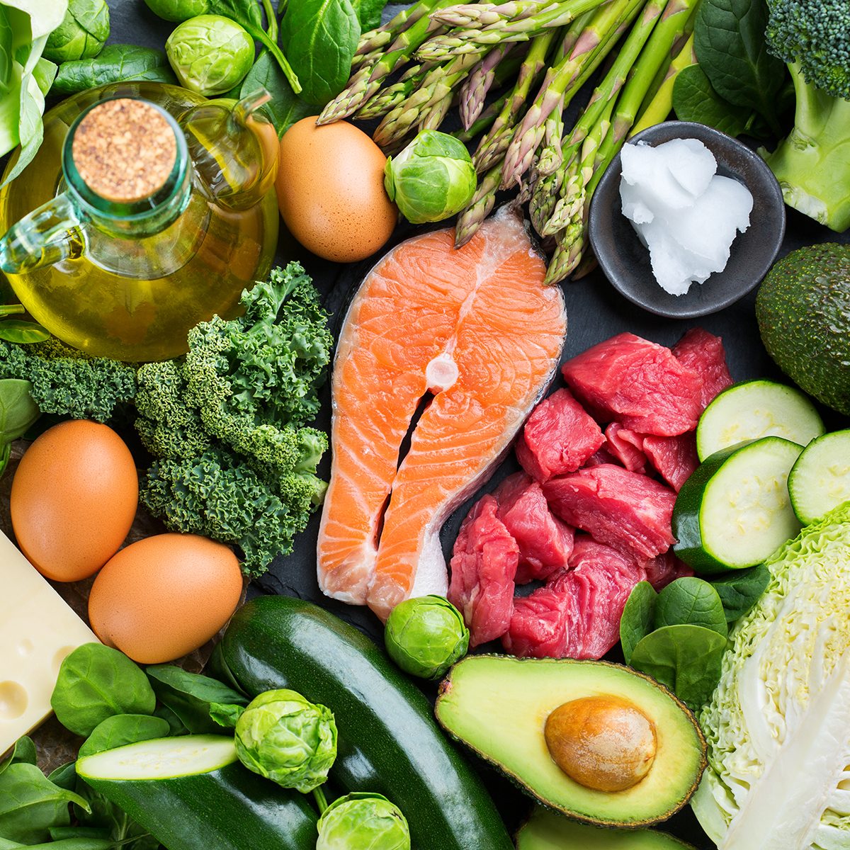 Balanced diet nutrition keto concept. Assortment of healthy ketogenic low carb food ingredients for cooking on a kitchen table. Green vegetables, meat, salmon, cheese, eggs. Top view background