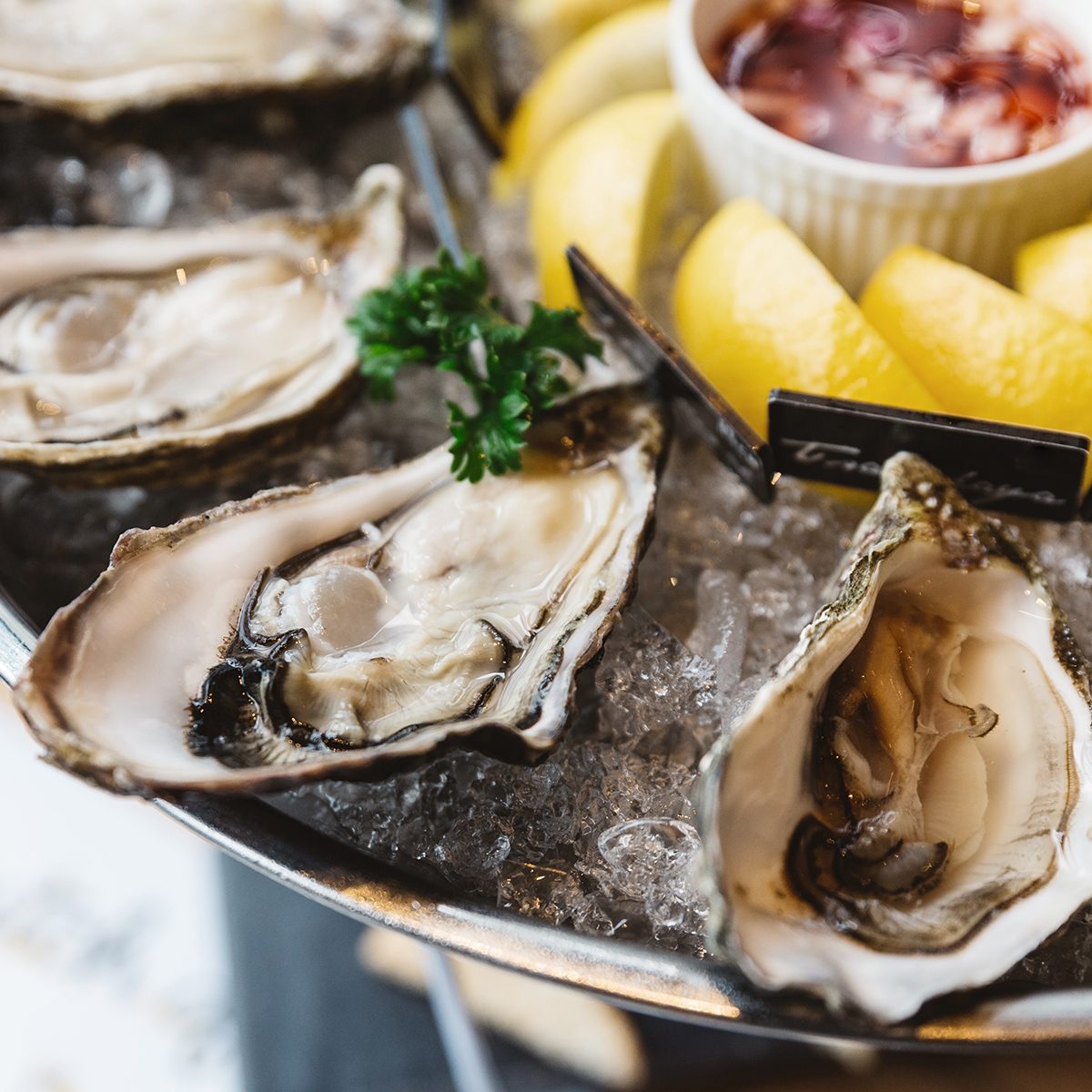Close up Fresh Oysters and many kinds of fresh oysters served in round tray with slice lemon and spicy sauce.