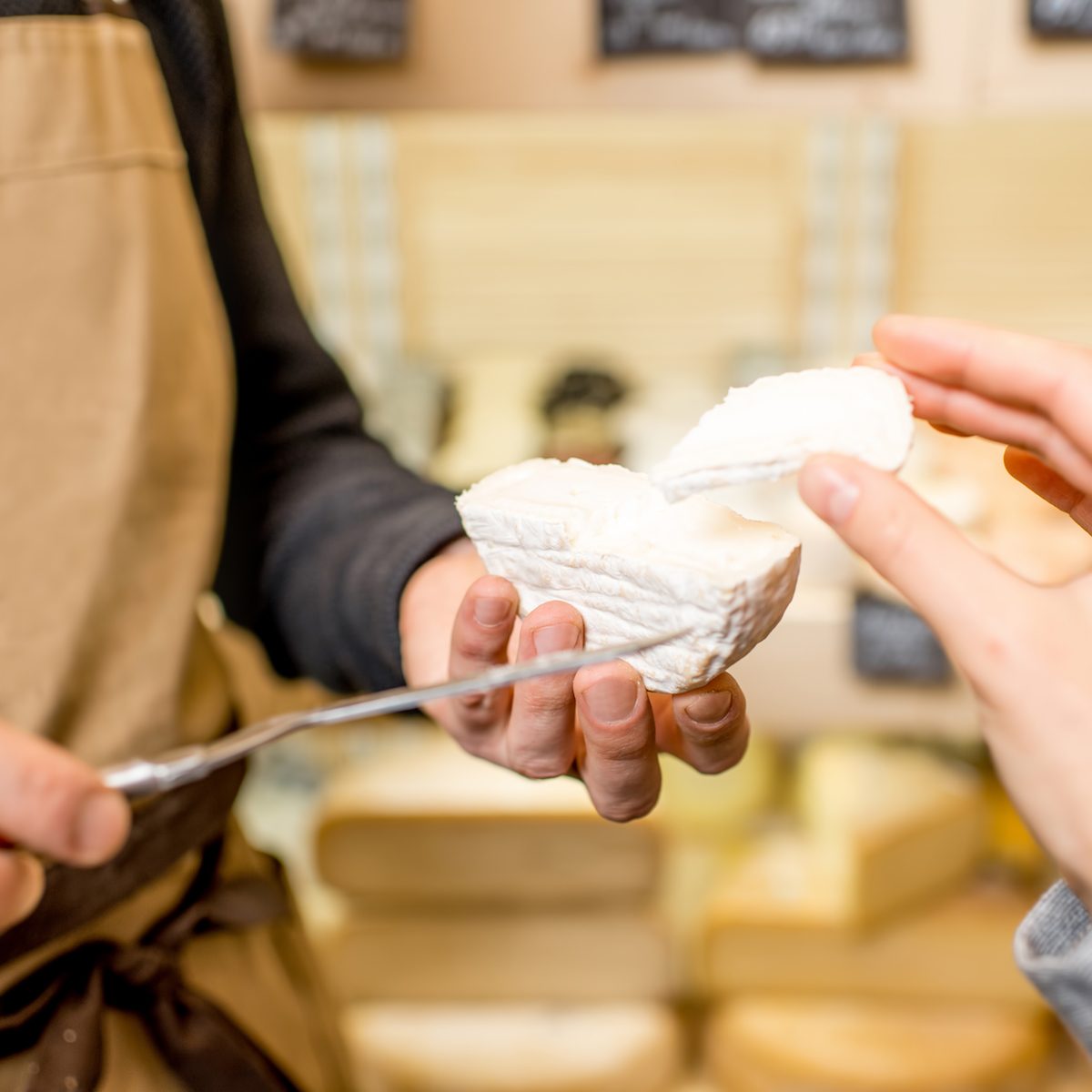 Cutting a cheese for woman customer at the food store