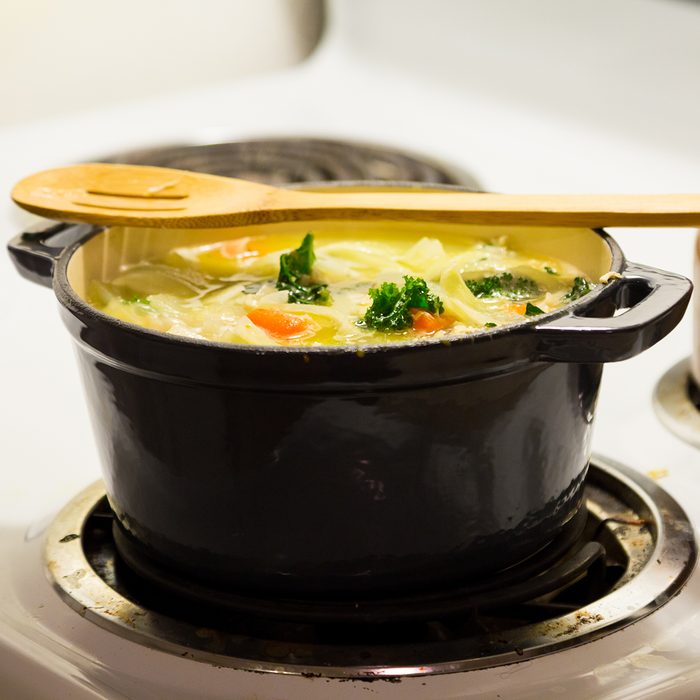 Dutch oven on a stove while cooking chicken noodle soup.