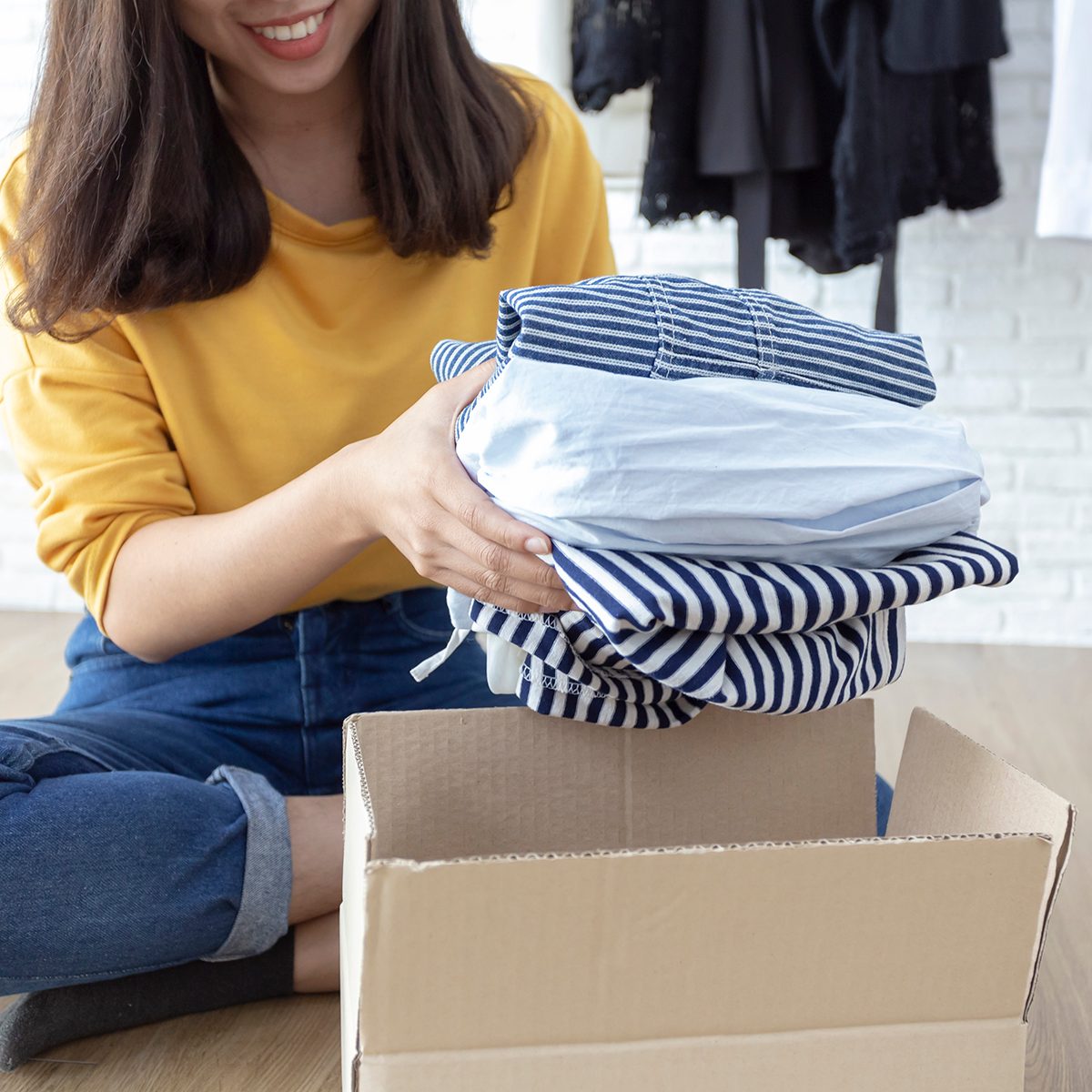 Woman holding Clothes with Donate Box In her room, Donation Concept.