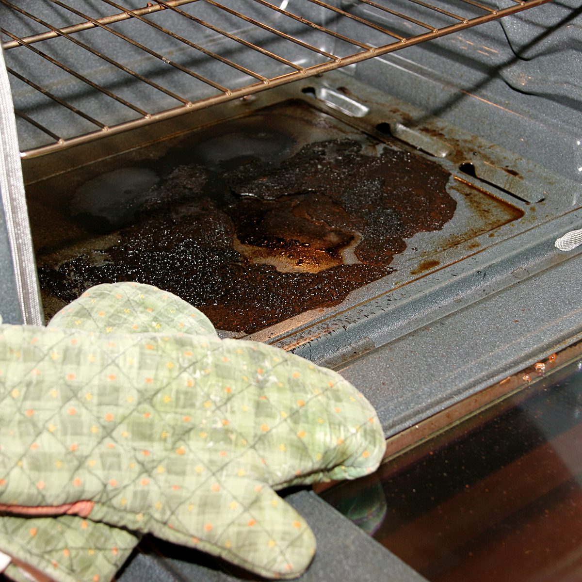 Badly burnt oven with oven mits in forefront