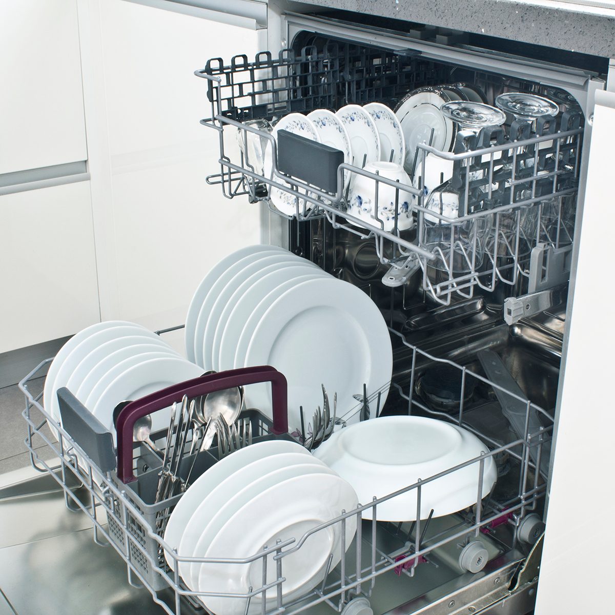 Open dishwasher with clean dishes in the white kitchen