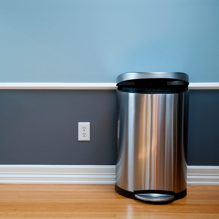Open trash can in empty room with wood flooring, blue wainscoting and a power outlet.