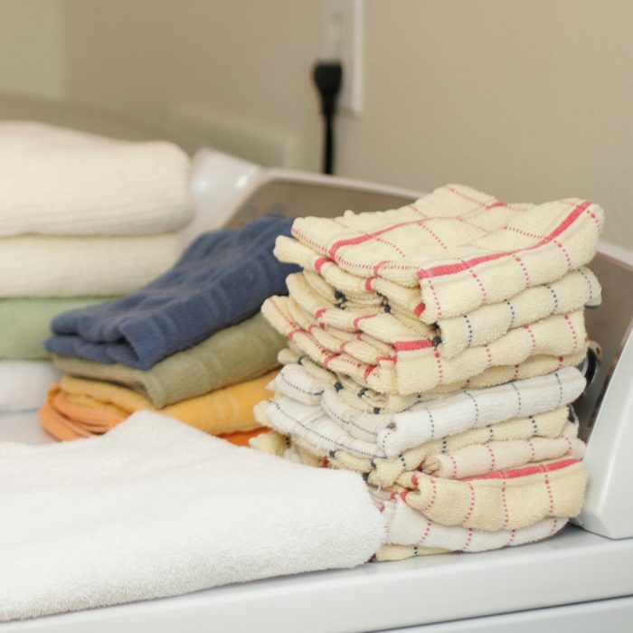 Arms and hands of a male folding towels onto a dryer and washer in a laundry room..