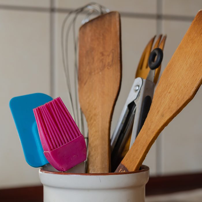 Silicone brush and wooden spatulas with tongs on the kitchen table. Eye level shooting. Close-up. Selective focus.