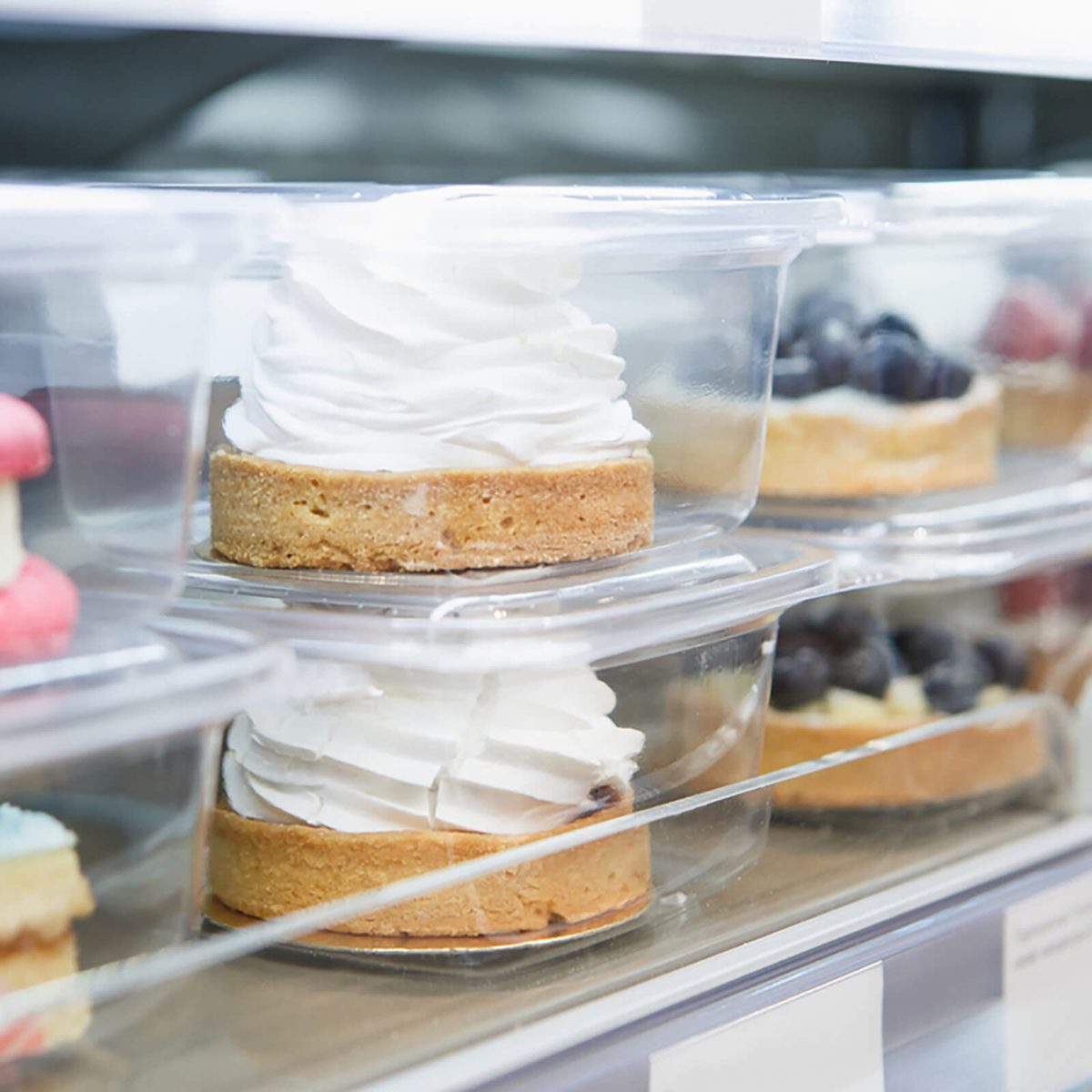 Delicious little cake in refrigerator packed in plastic container.Fresh sweet pastry for coffeebreak.Creamy cakes in freezer.Eat delicious bakery product with cream,sugar.Frozen cup cakes in container; Shutterstock ID 558665518