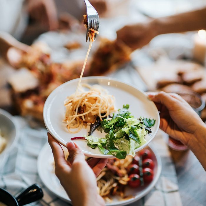 Group of joyful young Asian man and woman having fun, passing and sharing food across table during party