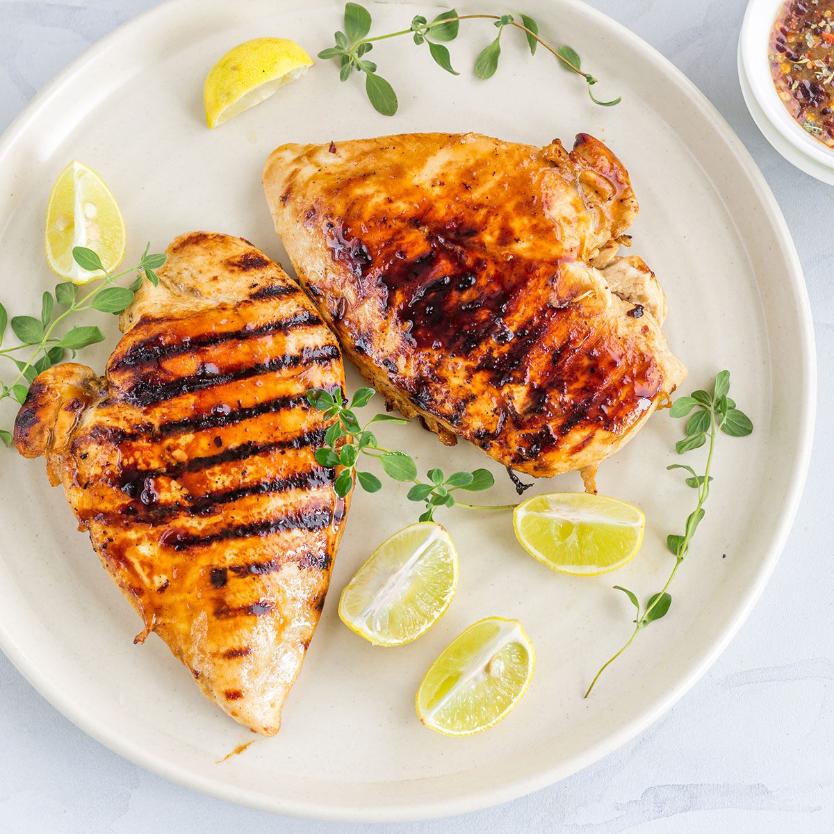 Grilled Chicken Breast on a White Plate with Lemon and Fresh Oregano.
