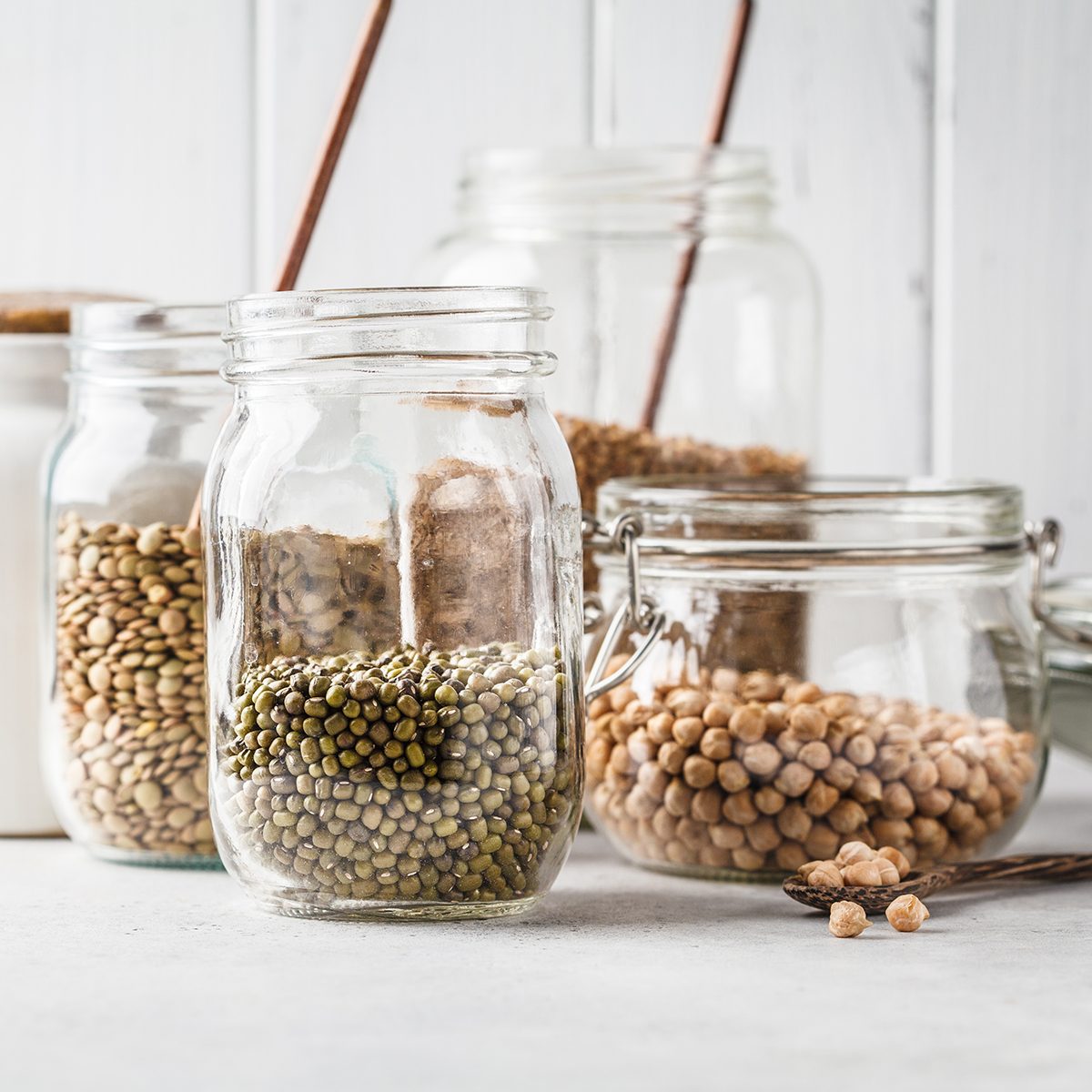 Various legumes: beans, chickpeas, buckwheat, lentils in glass jars on a white background. Healthy vegetarian food, vegetable protein, plant based diet concept.