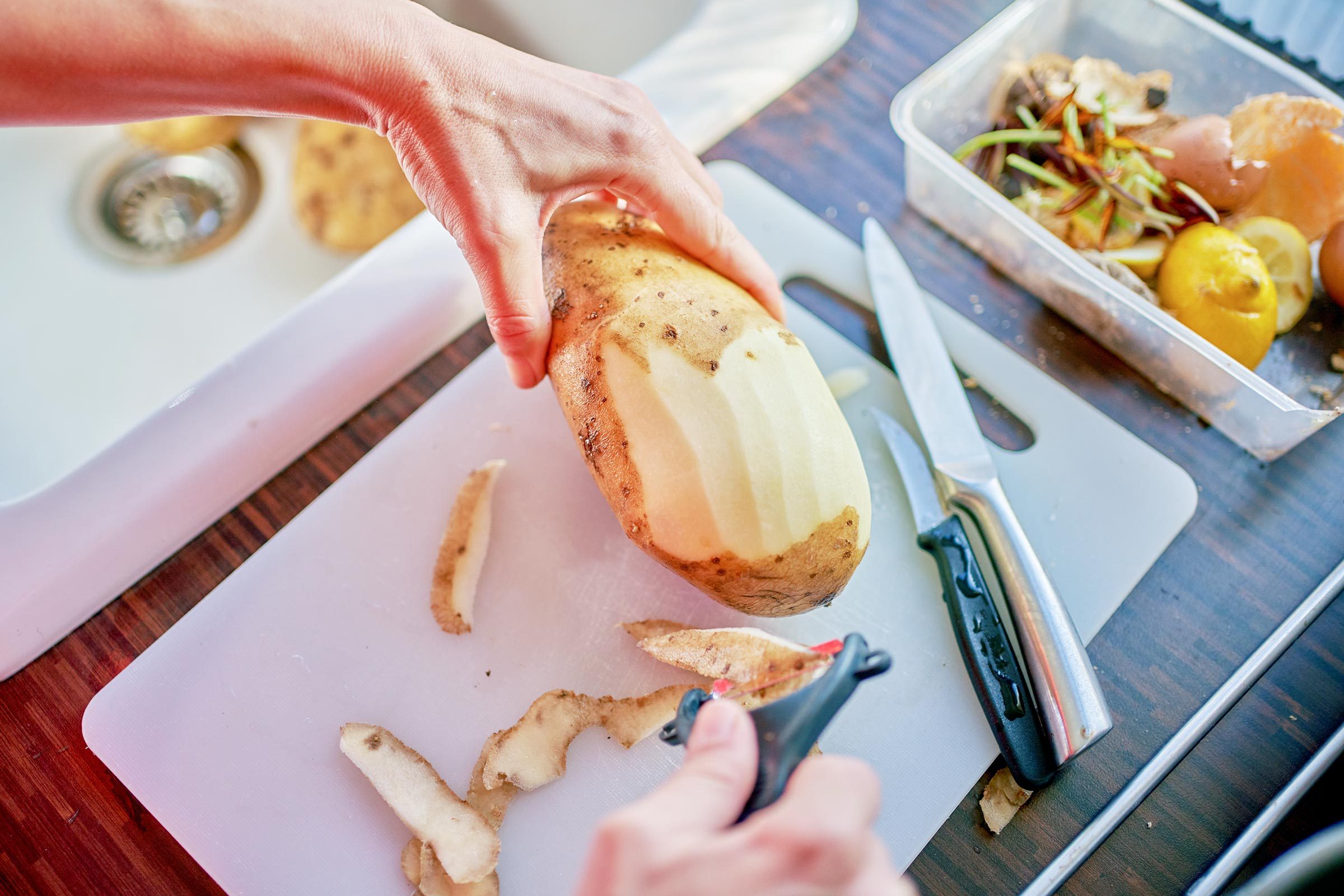 Peeling a potato next to a sink on wood kitchen countertop
