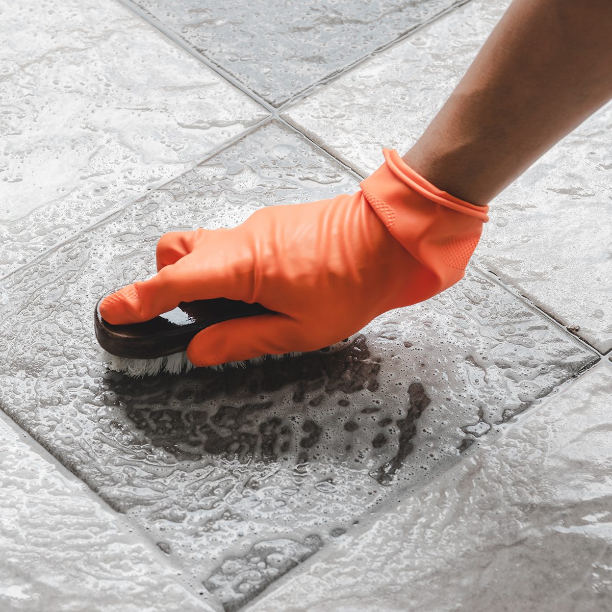 Hand of man wearing orange rubber gloves is used to convert scrub cleaning on the tile floor.
