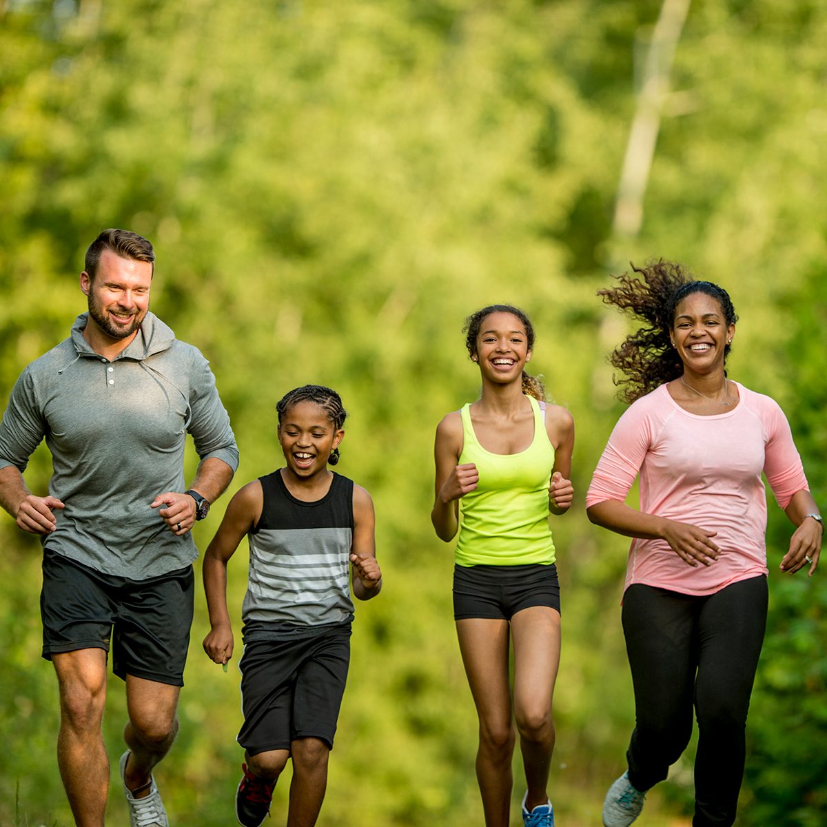 A multi-ethnic family (mother, father, son, daughter) getting exercise by going for a jog at the park.