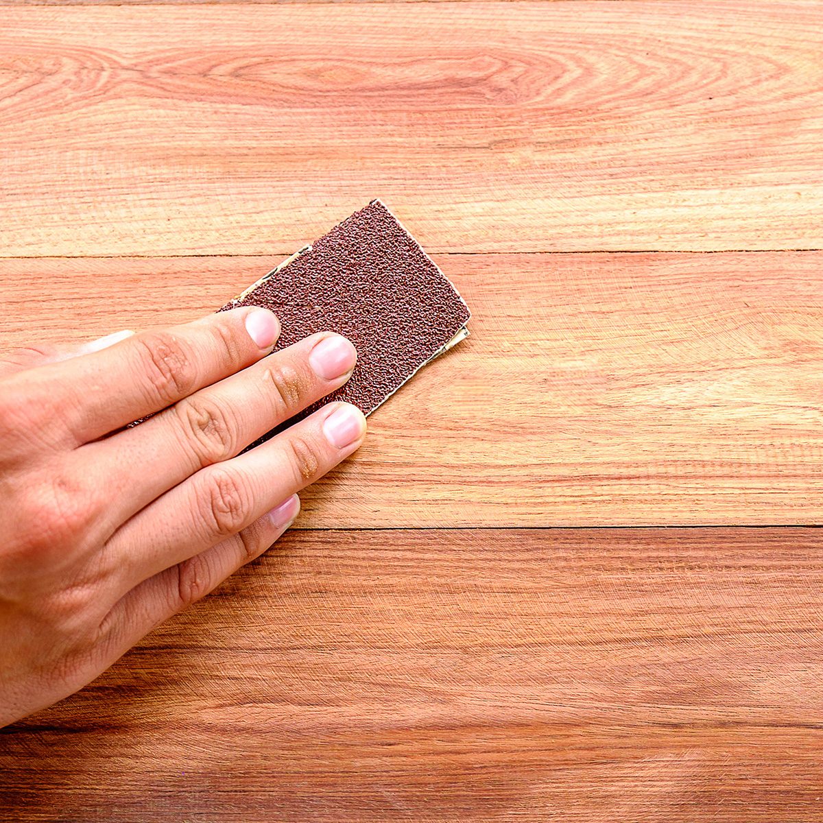 Cropped Hand Using Sand Paper On Wooden Table