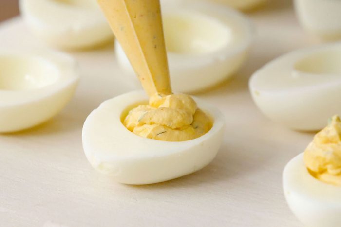 filling half of a hard boiled egg with deviled egg mixture
