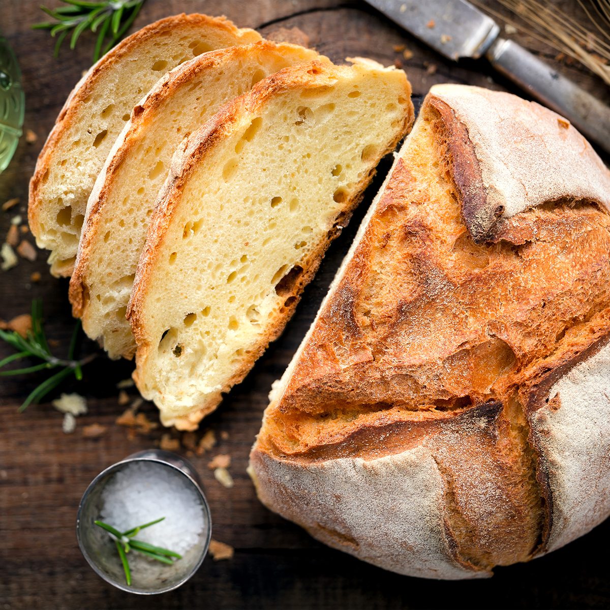 Rustic loaf of homemade bread served with olive oil, rosemary and salt on dark wooden table. Overhead view