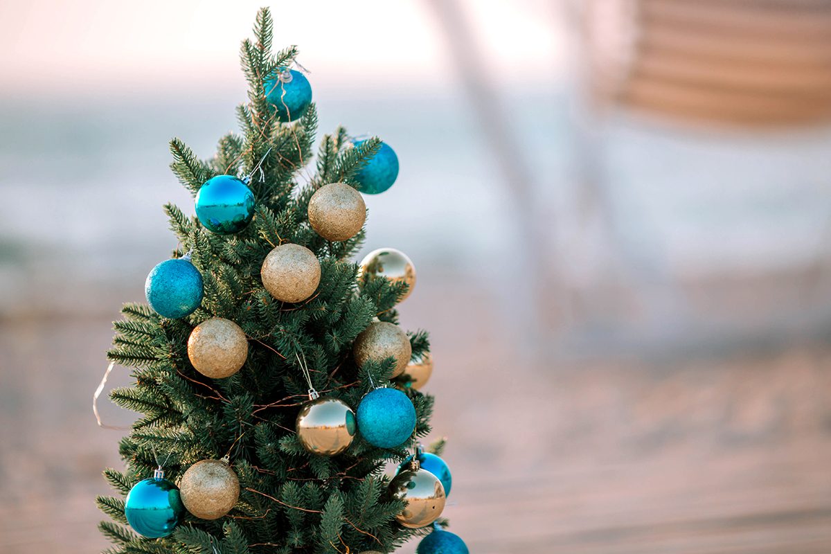 Christmas Tree Decorated With Gold And Blue Balls On A Sea Sandy Beach.
