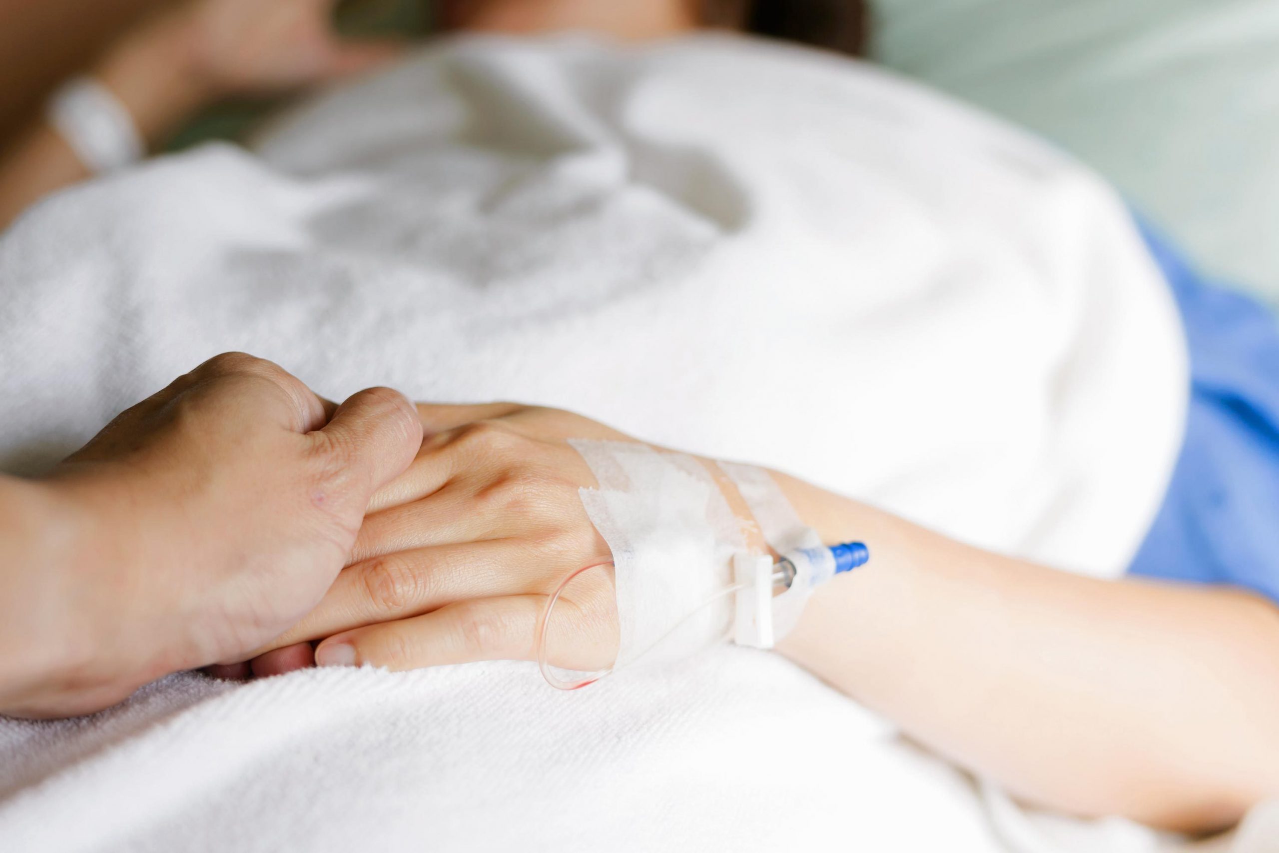 holding the hand of a person undergoing chemo treatment