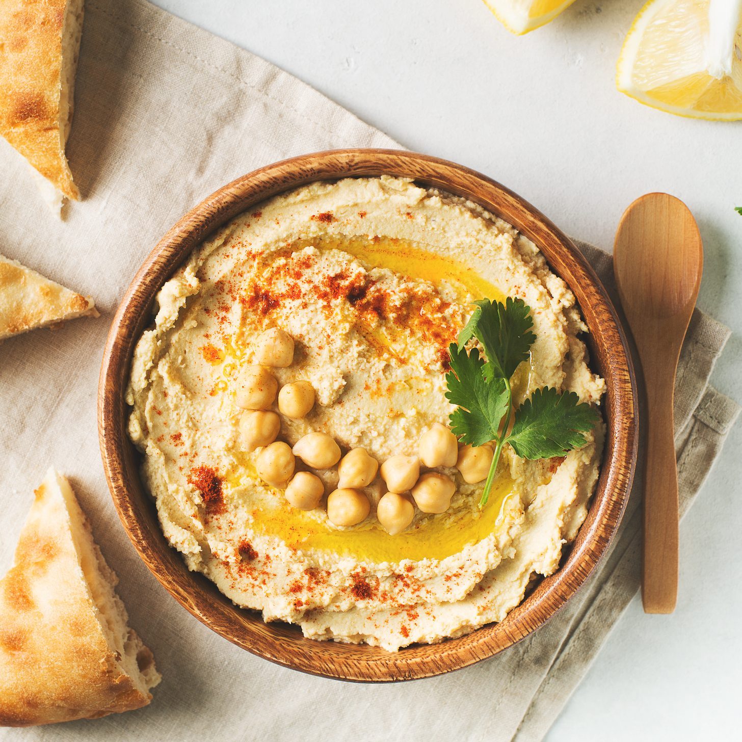 Hummus dip with chickpea, pita and parsley in wooden plate on white background