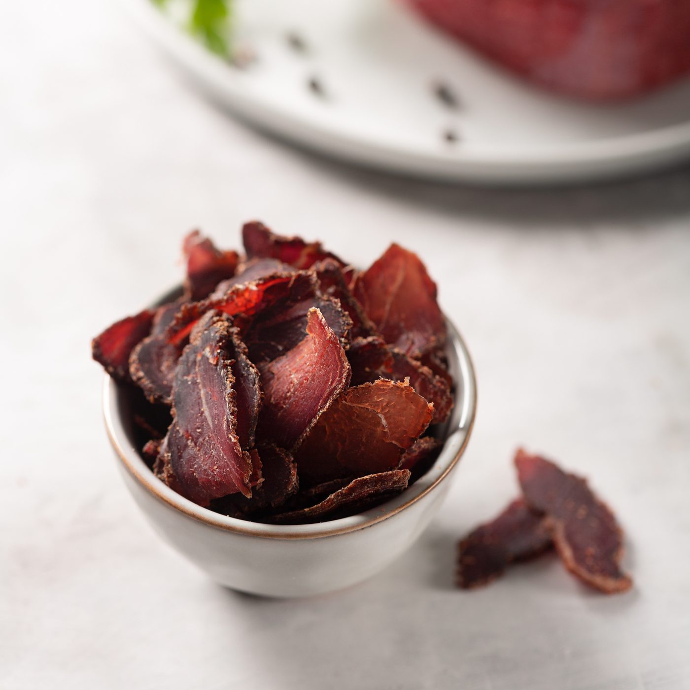 Bowl with jerky meat and raw beef on gray concrete background