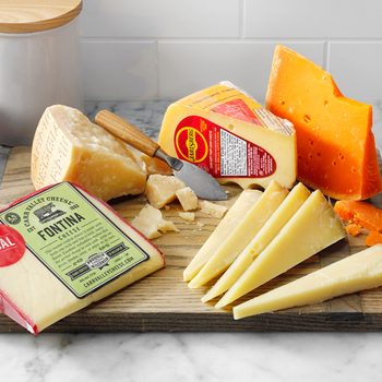 variety of cheeses on a cutting board on a kitchen counter