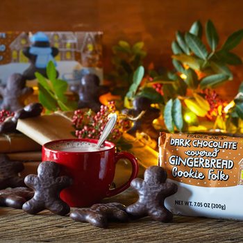Dark Chocolate Gingerbread Cookie Folk with lights, greenery and wrapped packages, mug of hot chocolate and cookies scattered on surface