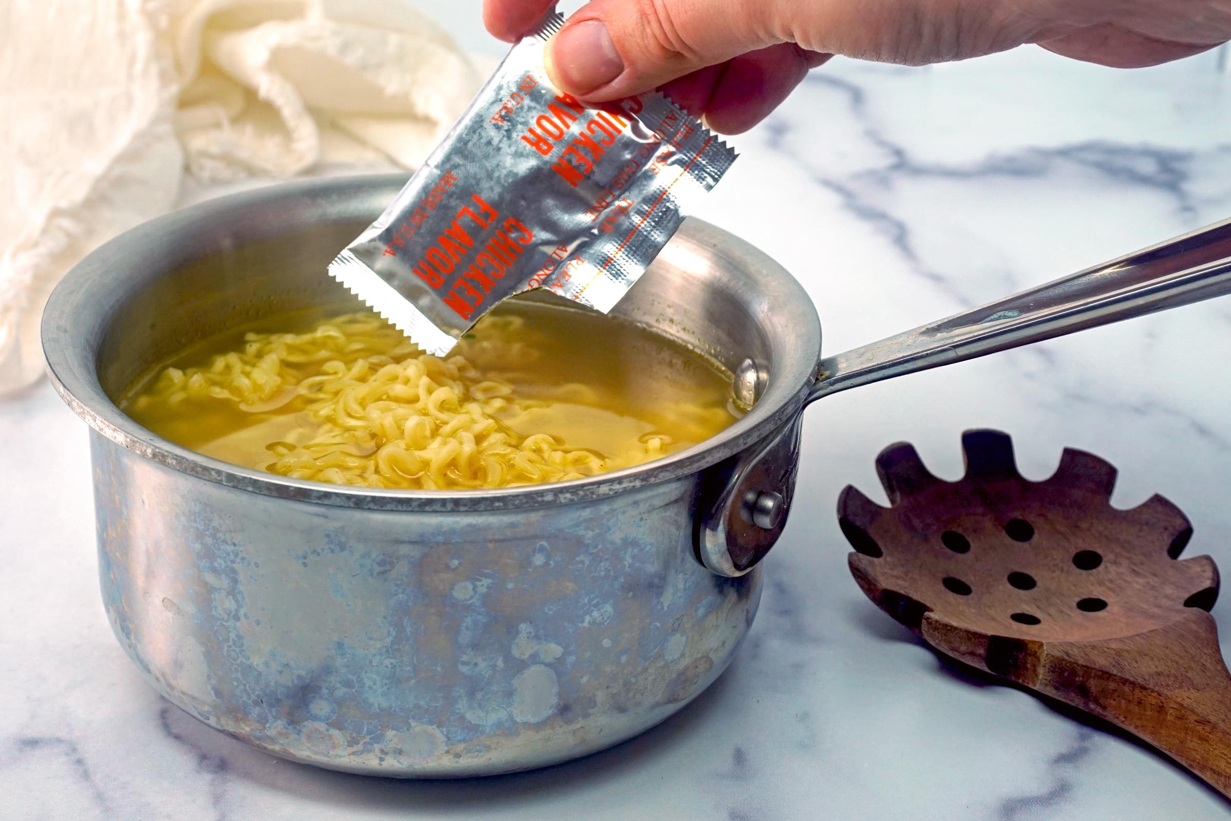 Cheesy Ramen cooked noodles in a pot with hand adding flavor packet seasoning