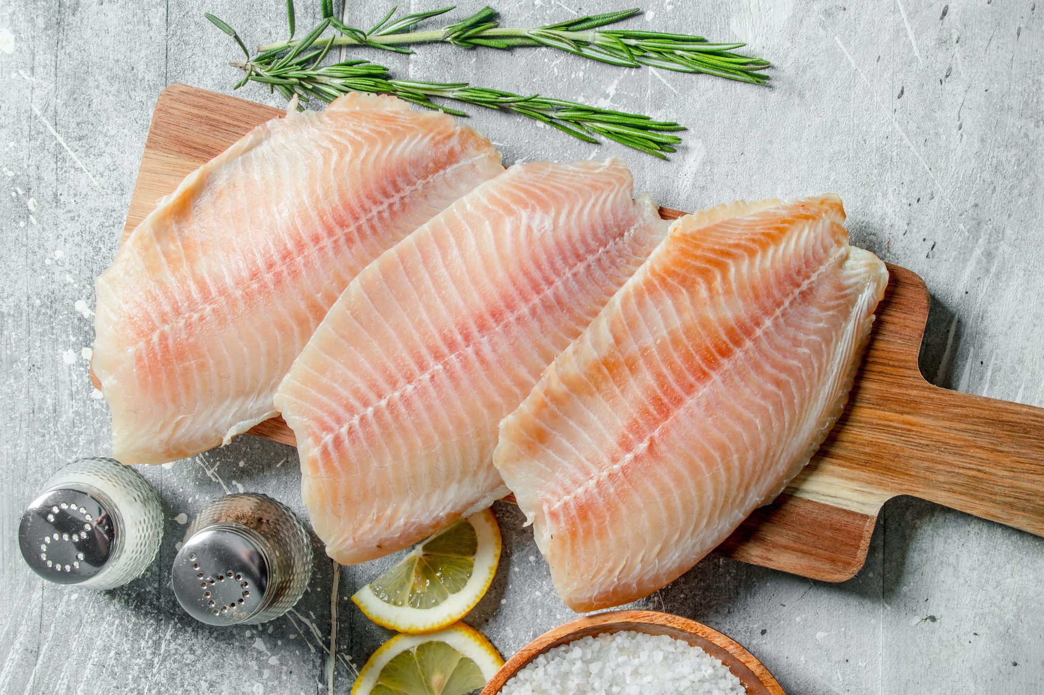 Fish fillet on a wooden cutting Board with rosemary, spices and lemon slices.