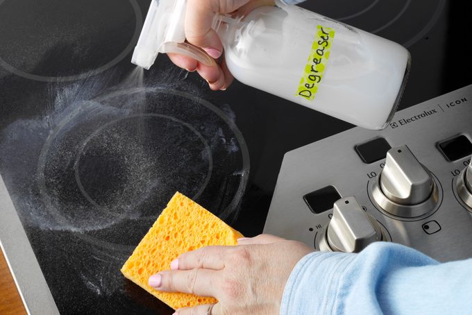 hand spraying degreaser onto a glass stovetop
