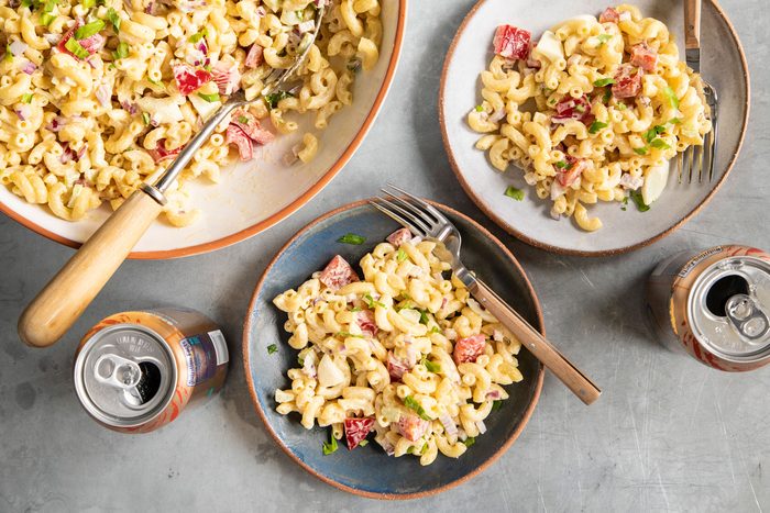 Macaroni Salad in a large bowl with some served into two smaller bowls nearby