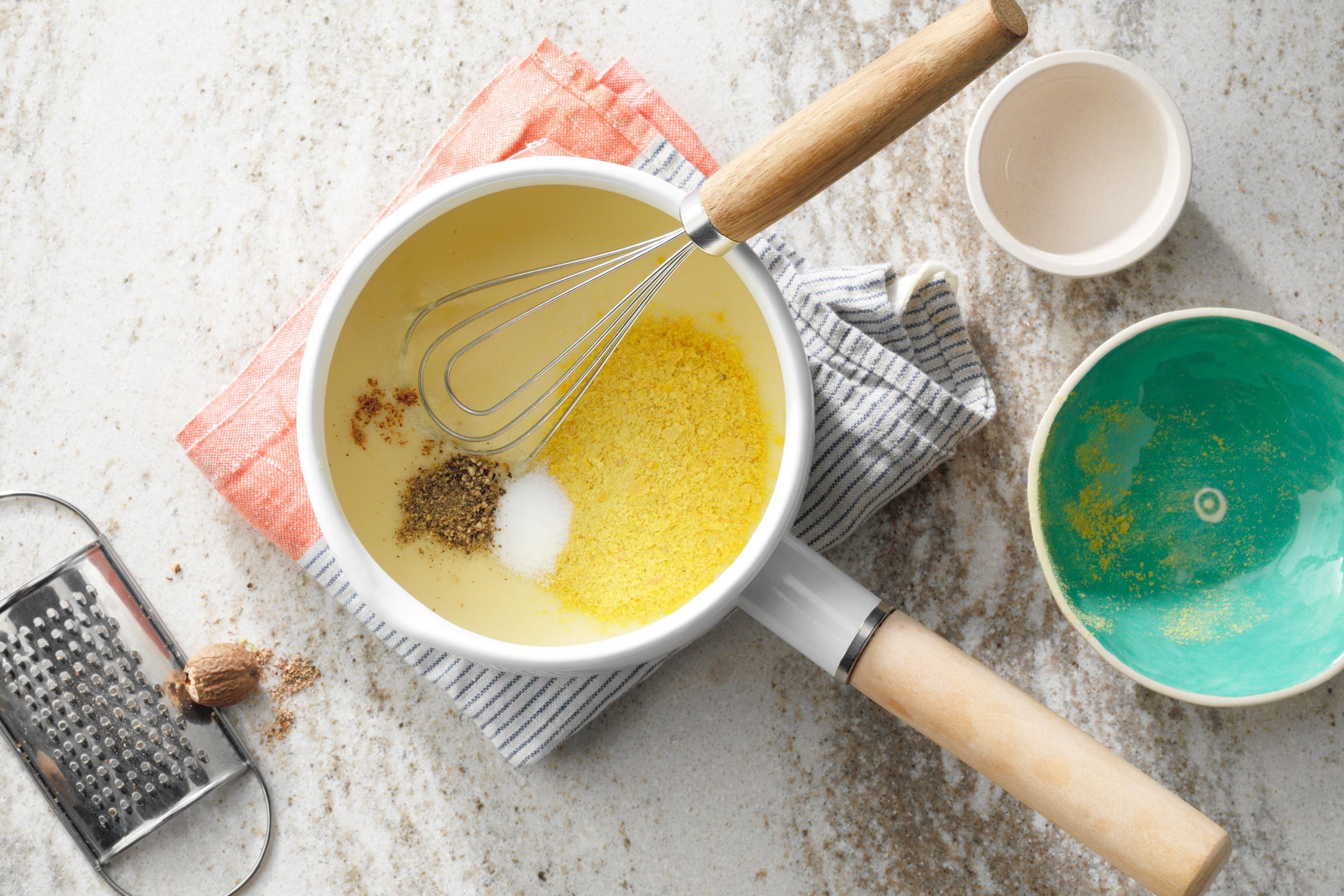 sauce in a pot with sprinkles of seasoning and a whisk resting on the edge