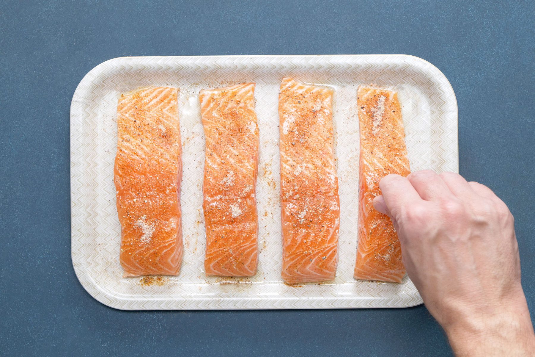 A person Sprinkling the seasoning mixture evenly on salmon fillets