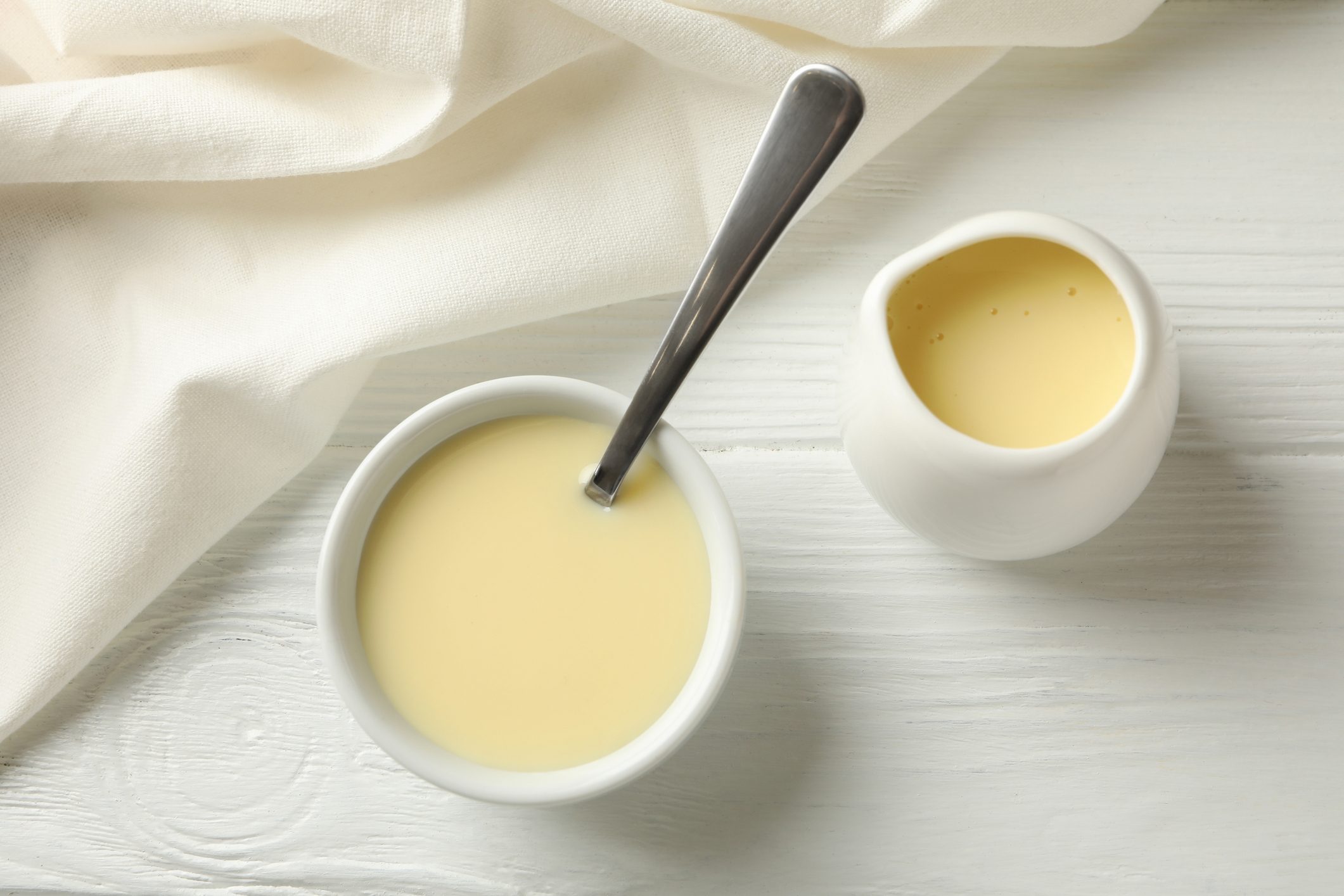 Kitchen towel and bowls with condensed milk on wooden background