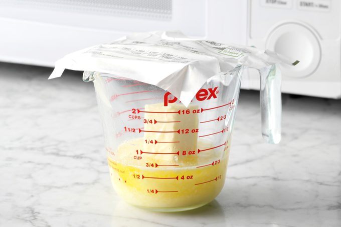 Melting Butter in a glass measuring cup With a butter Wrapper on top sitting on the counter, a microwave is nearby in the background