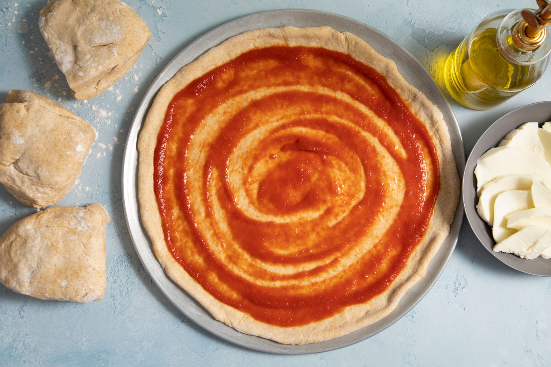 Sauce on pizza base with cheese and oil on side